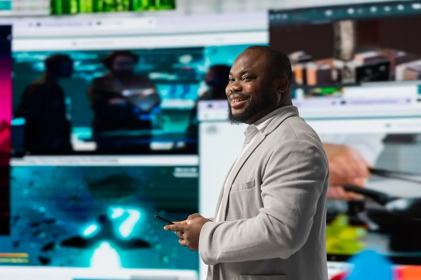 Веселый мужчина листает ленту соцсетей на смартфоне перед цифровой видеостеной, демонстрирующей ...